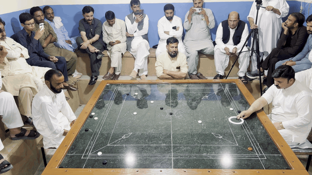 Pakistani carrom shot 3: the striker and pieces glide across the marble board.
